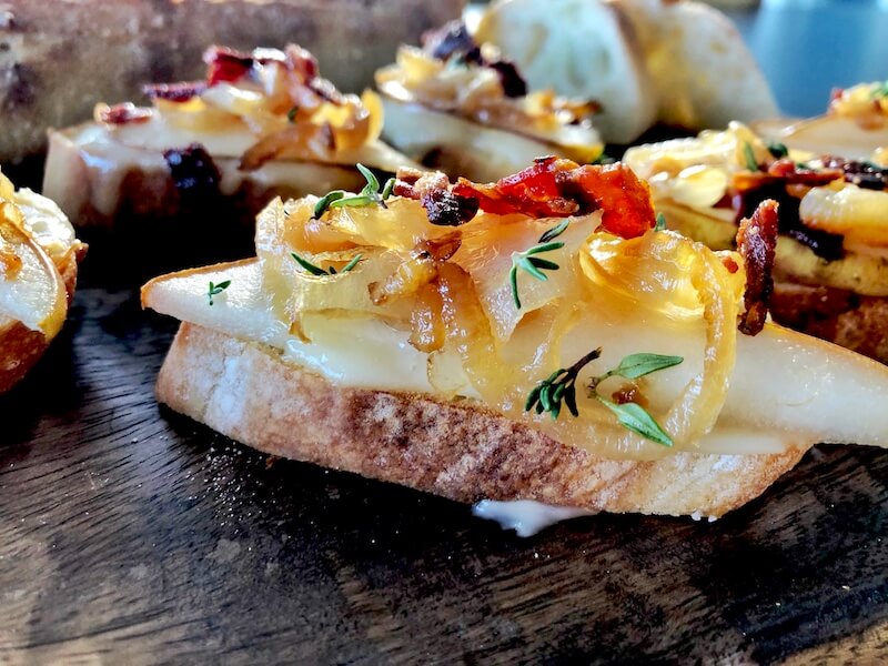 close up angled crostini with cheese, pear, onions and bacon